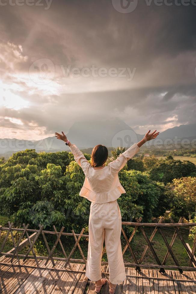 Asian woman enjoying raised hands on terrace and Doi Luang Chiang Dao mountain view at the sunset photo
