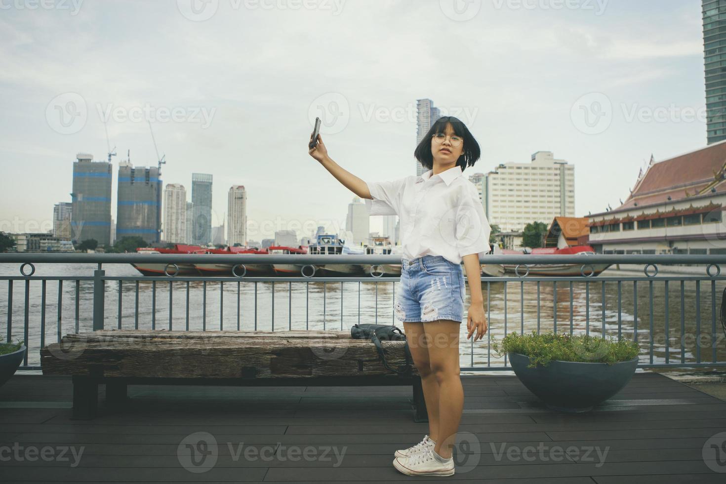 Adolescente asiático tomando fotos por teléfono inteligente, de pie en las calles de la ciudad