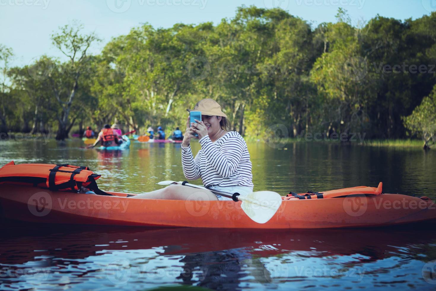 Mujer joven tomando fotos por teléfono móvil mientras navega en kayak de mar
