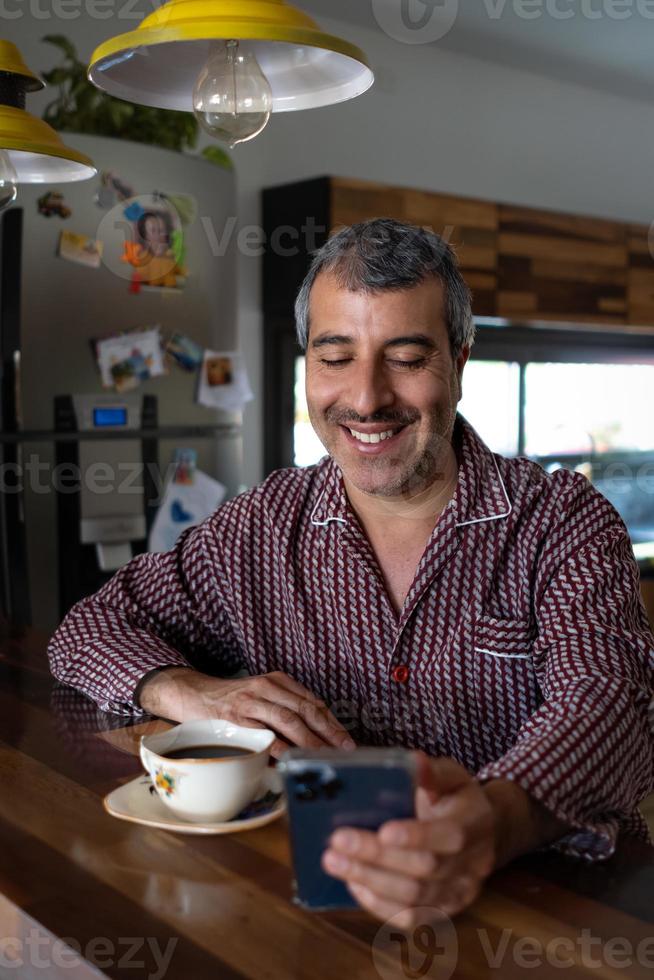 Hombre en pijama desayunando mirando su teléfono celular foto