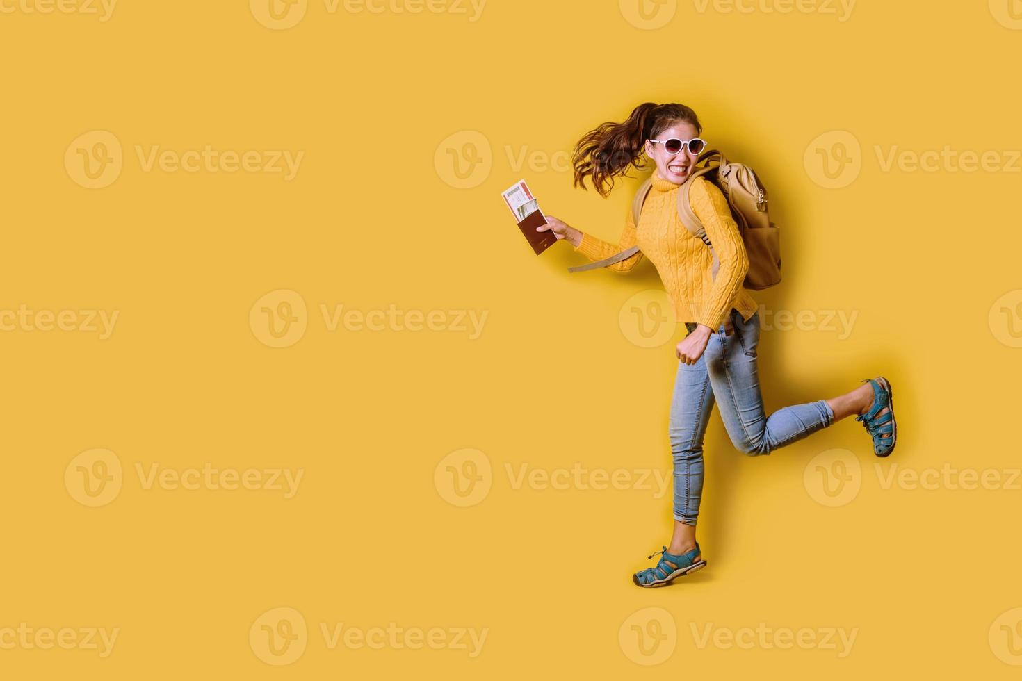 Woman traveler with suitcase, holding passport with ticket on Yellow background. Portrait of smiling happy girl in the yellow dress. people traveler photo