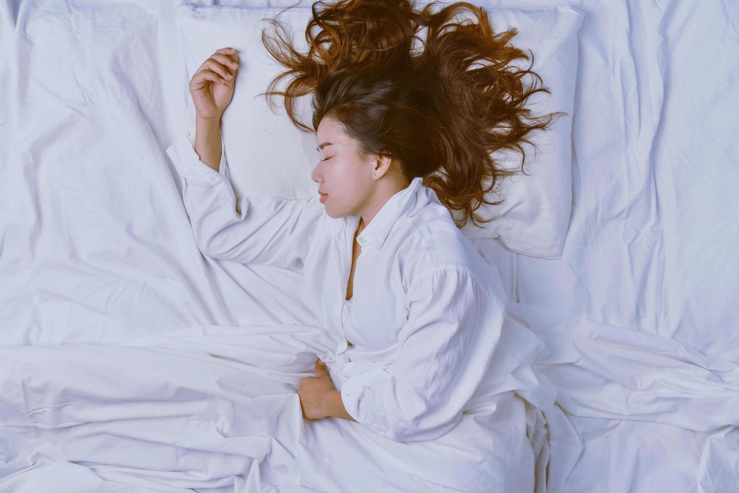 mujer joven durmiendo en la cama. Vista superior de la mujer joven acostada durmiendo bien en la cama. durmiendo relajarse, joven sonriente bonita dama yace en la cama. foto