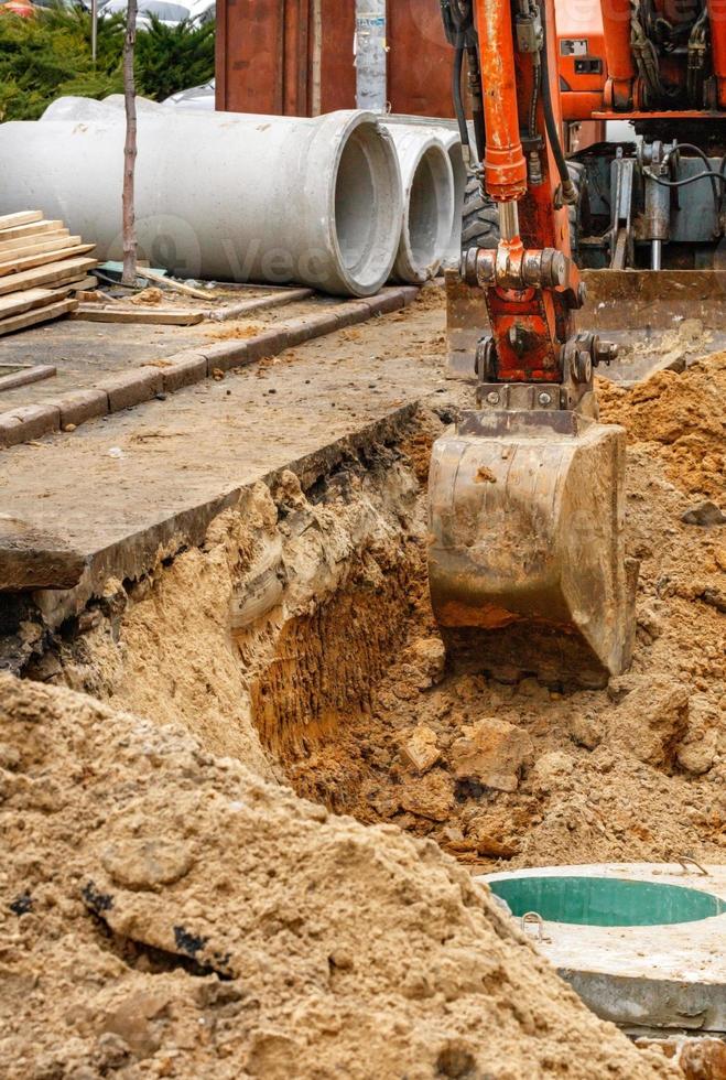 A bucket of a heavy construction excavator digs a trench while repairing a city collector on the roadway. photo
