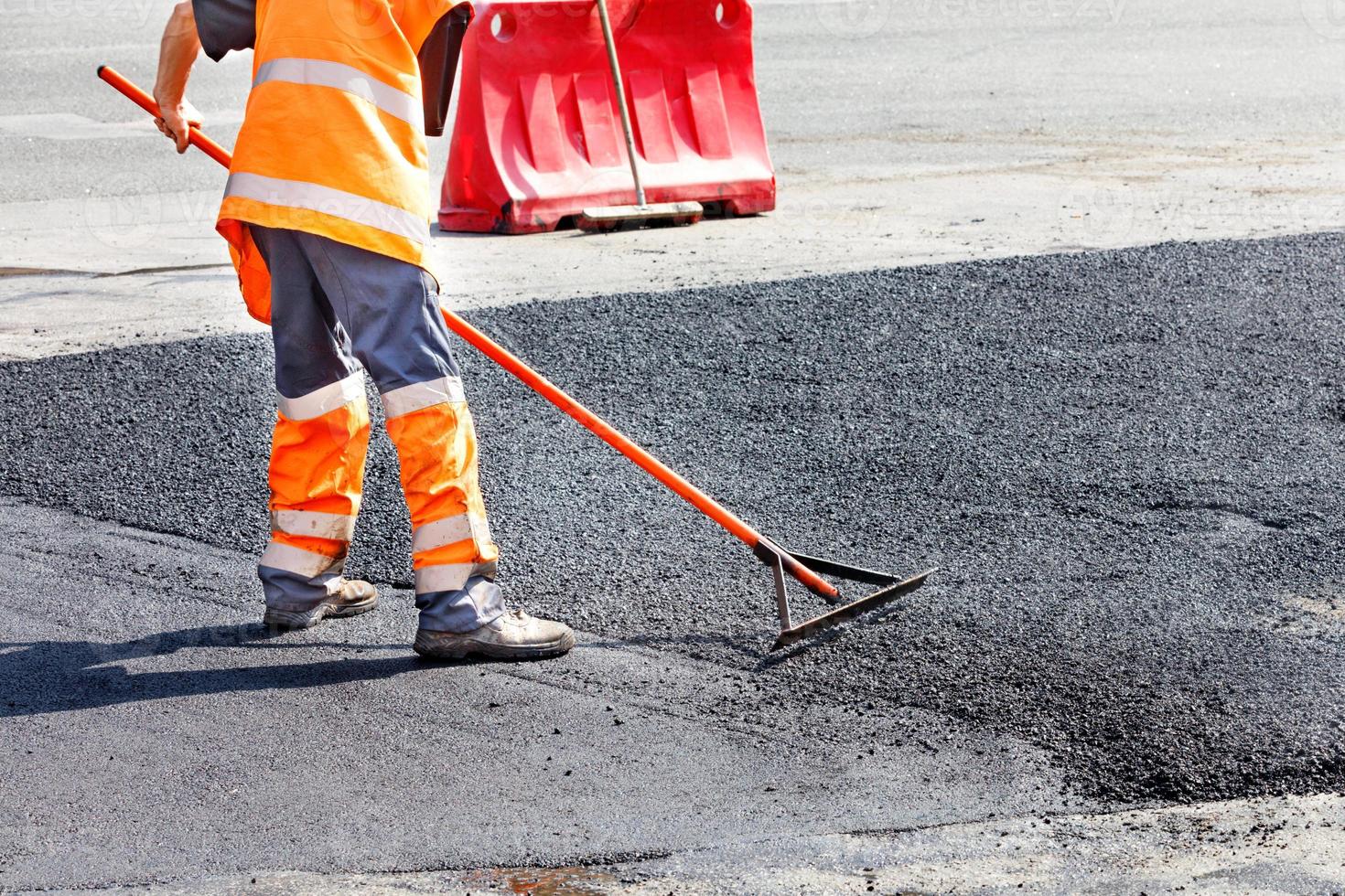 un trabajador del servicio de carreteras alisa el asfalto caliente con un nivel de metal manualmente cuando repara una carretera. foto