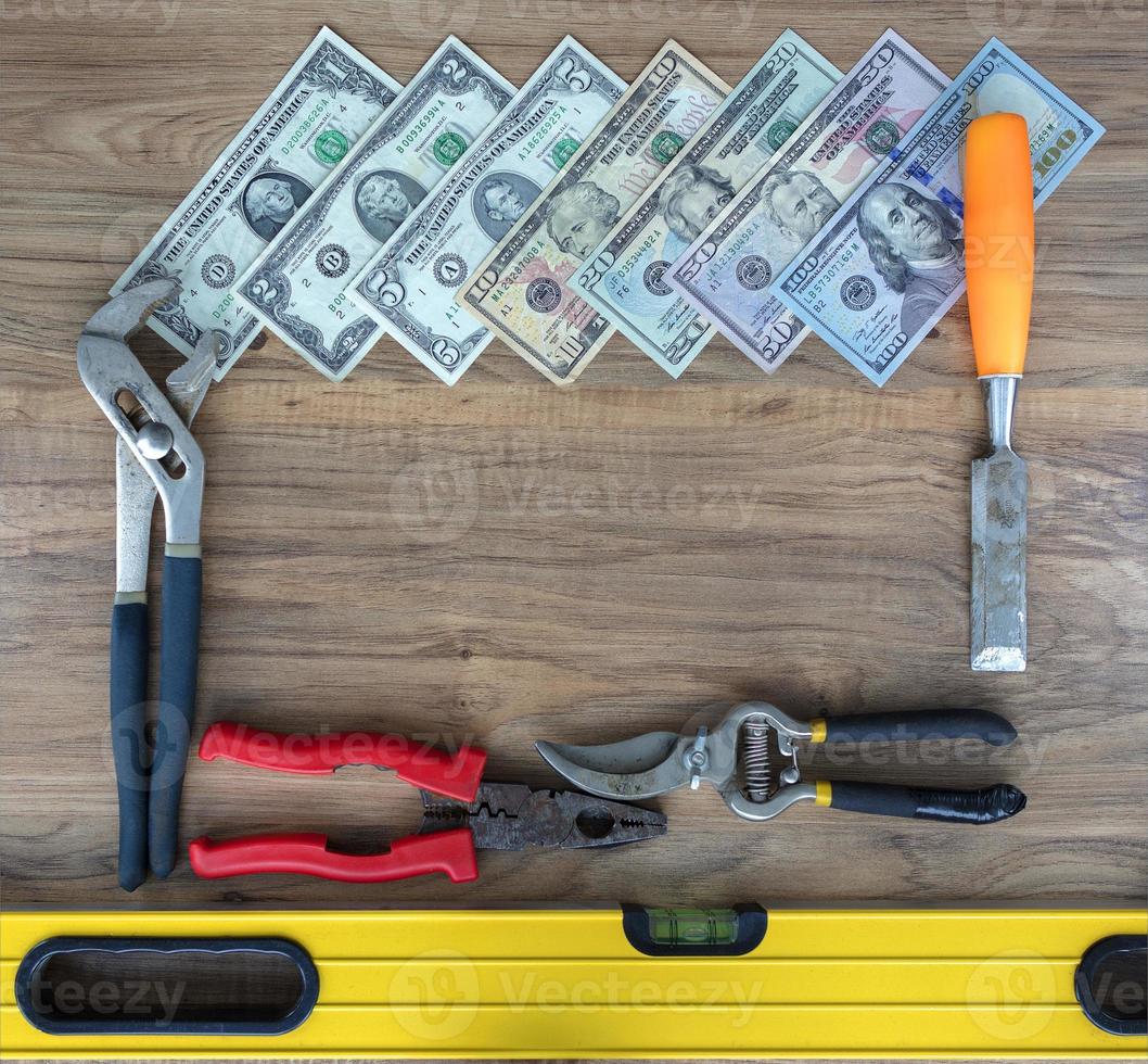 Old construction tools and a set of dollar bills on a wooden table close-up photo