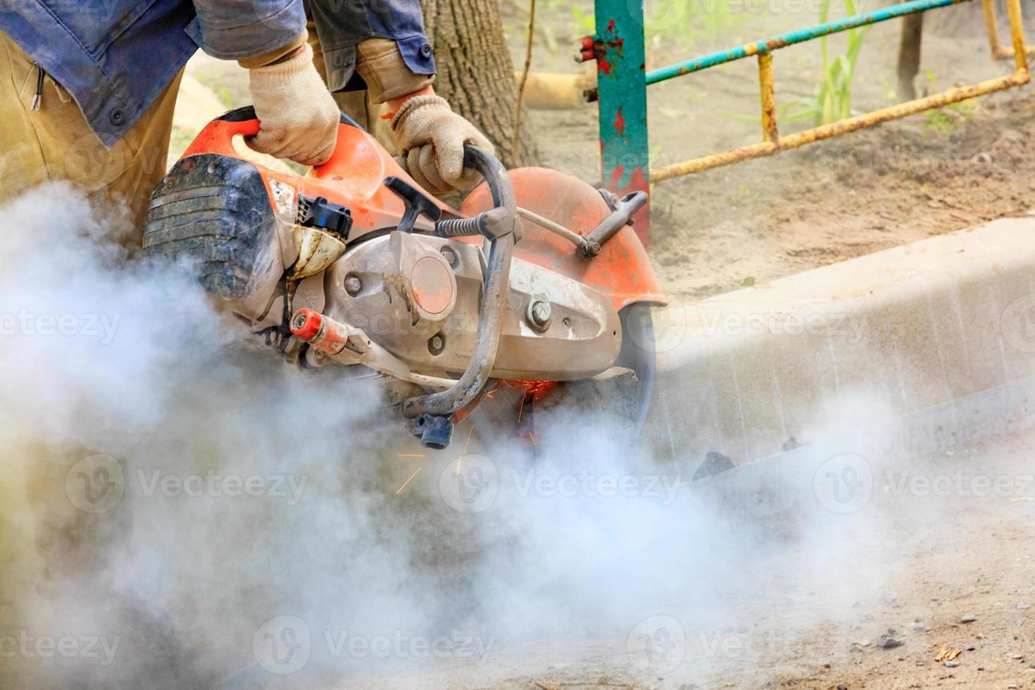 un trabajador de la construcción que usa una sierra de gasolina portátil corta un bordillo de concreto para reparar una calzada. foto