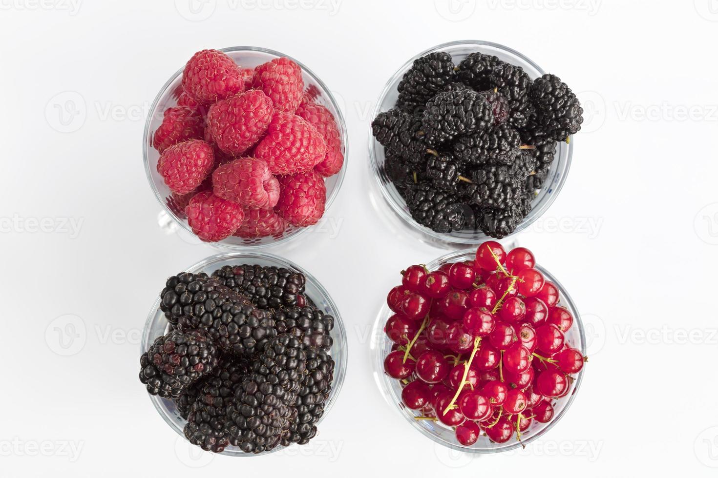 Raspberry, a big black blackberry, red currant and mulberry are located in clear glass on a light background photo