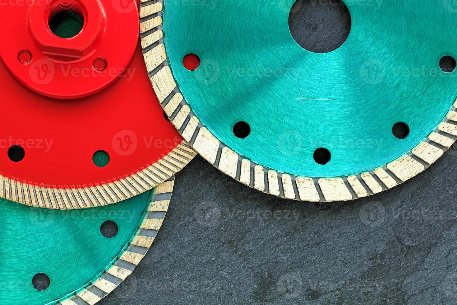Several diamond cutting wheels of red and emerald color against a background of gray granite. photo