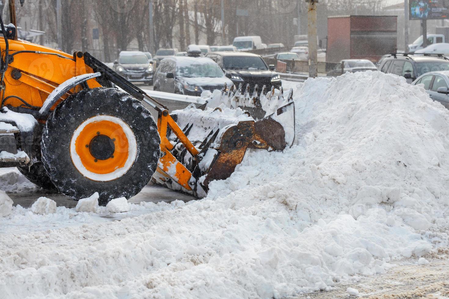 un gran cucharón de una topadora amarilla quita la nieve de una carretera de la ciudad durante una nevada. foto