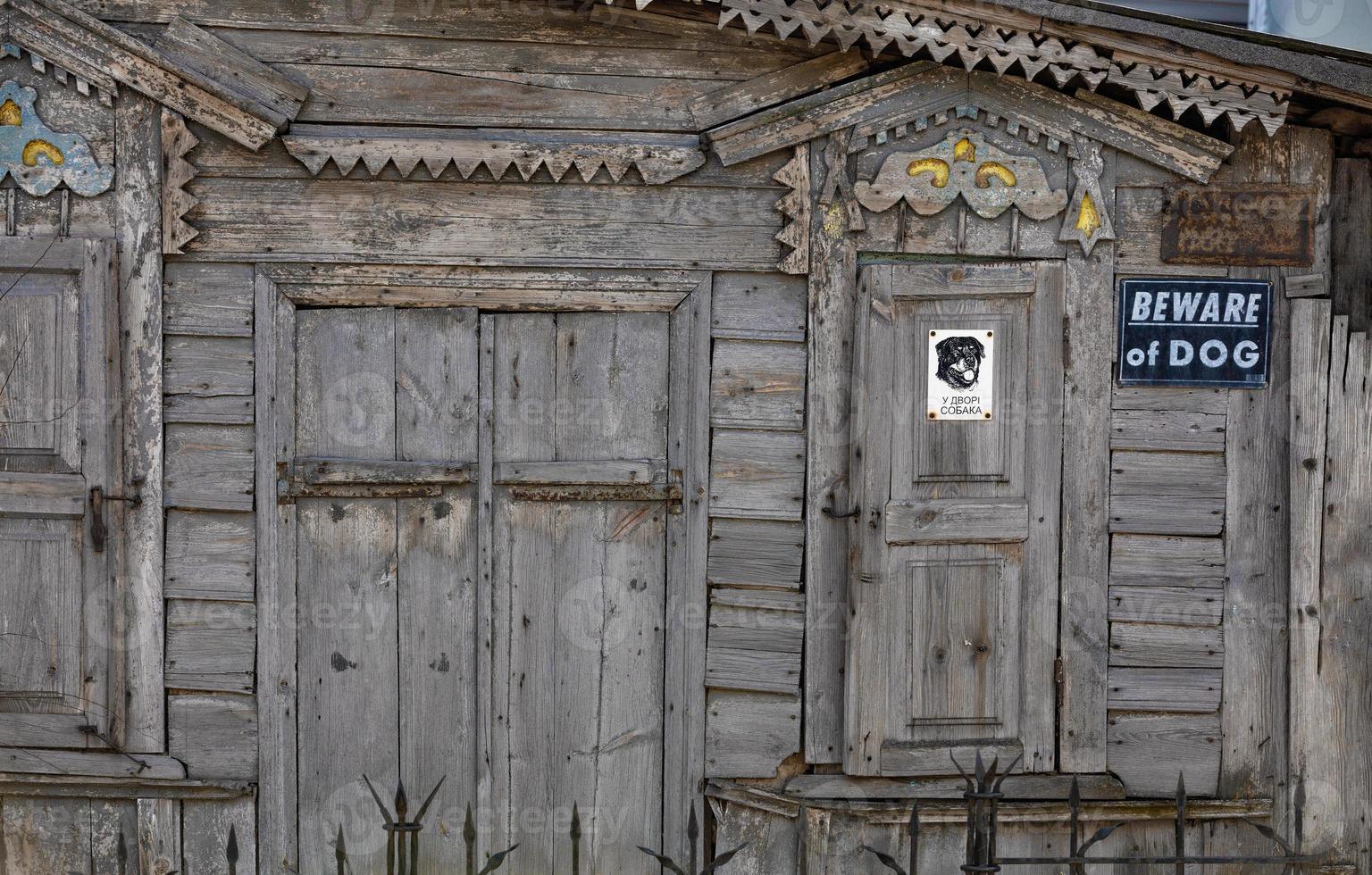 Part of the wooden facade of an old dilapidated house with carved platbands, curly wall elements and metal bars with a Beware of dog sign. photo