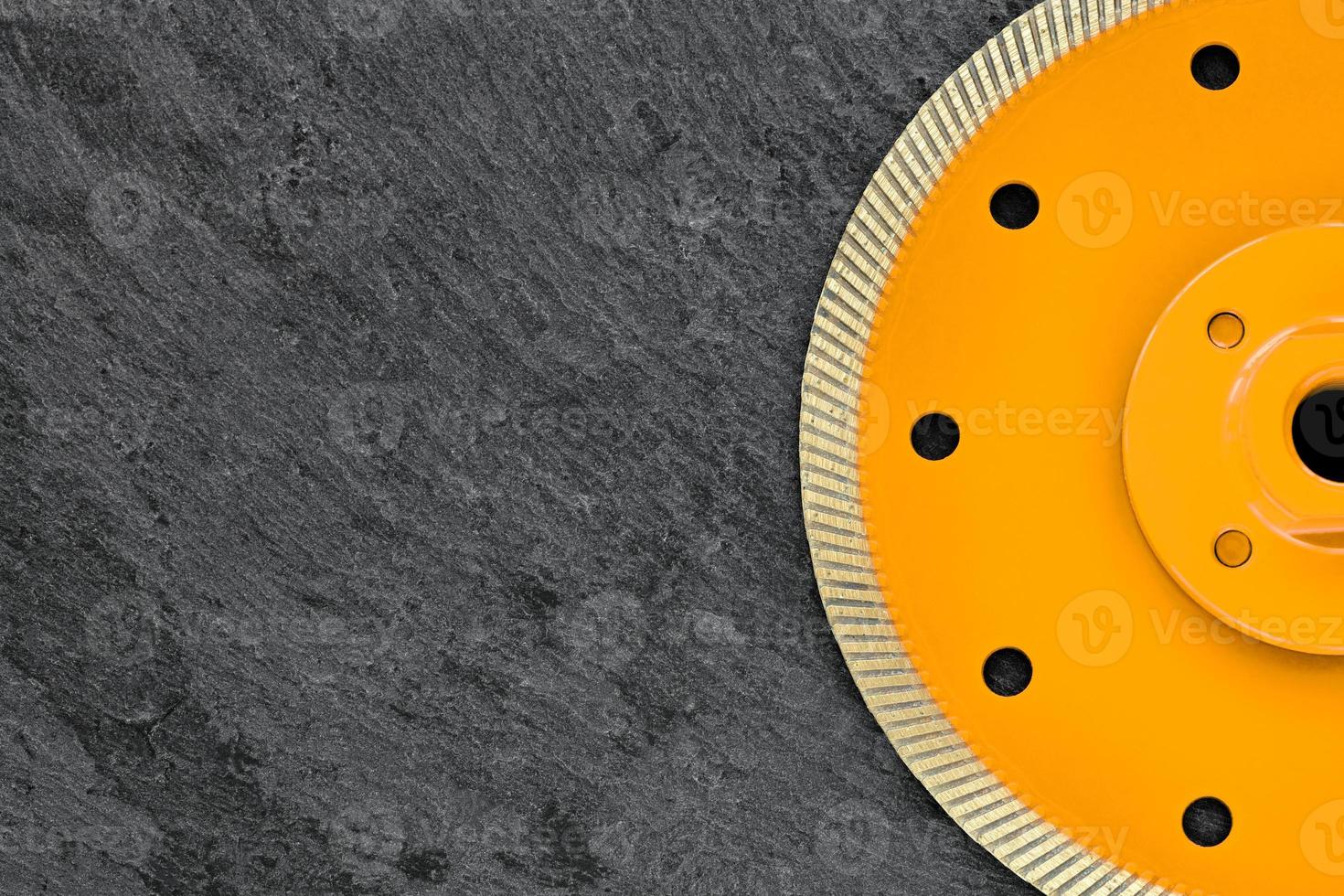 Half of a yellow diamond cutting wheel with a threaded nut on a dark gray granite background, the concept of stone processing in the interior and construction. photo