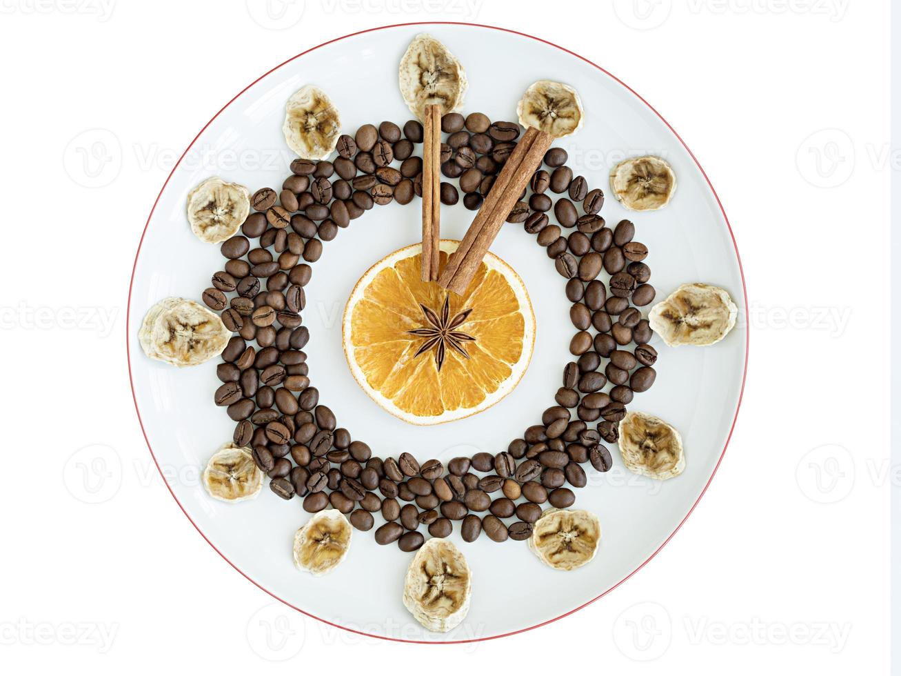 Grains of roasted coffee, mugs of dried orange and banana, cinnamon stick, anise star lie on a porcelain plate in the form of a clock photo