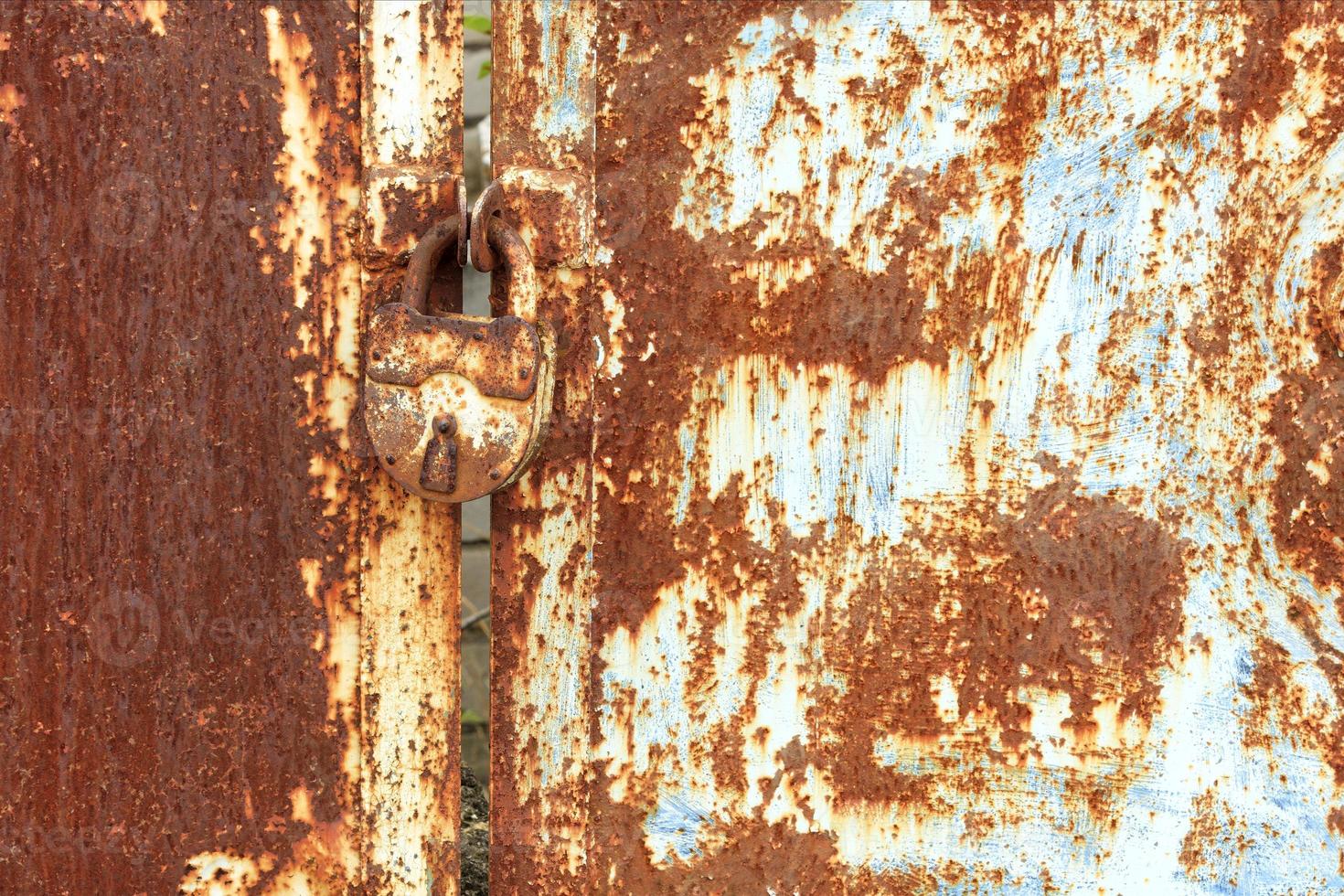 An old rusty lock connects a rusty gate. Rust on old metal sheet texture. photo