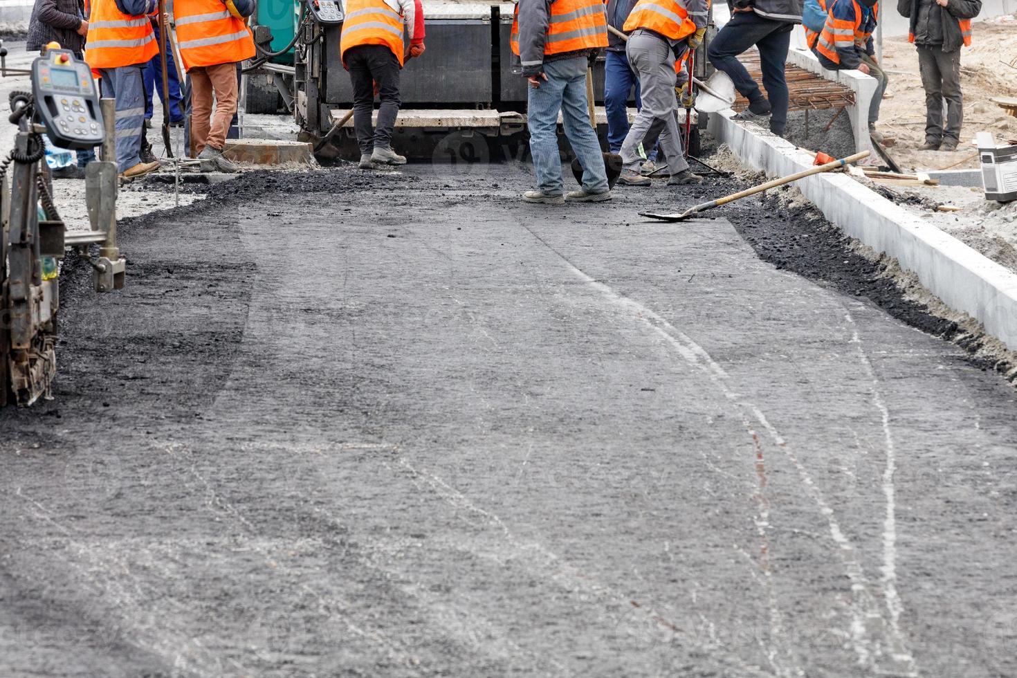 un grupo de trabajo de trabajadores de la carretera distribuye uniformemente la primera capa de asfalto caliente con palas manualmente sobre el tramo de la carretera que se está reparando. foto