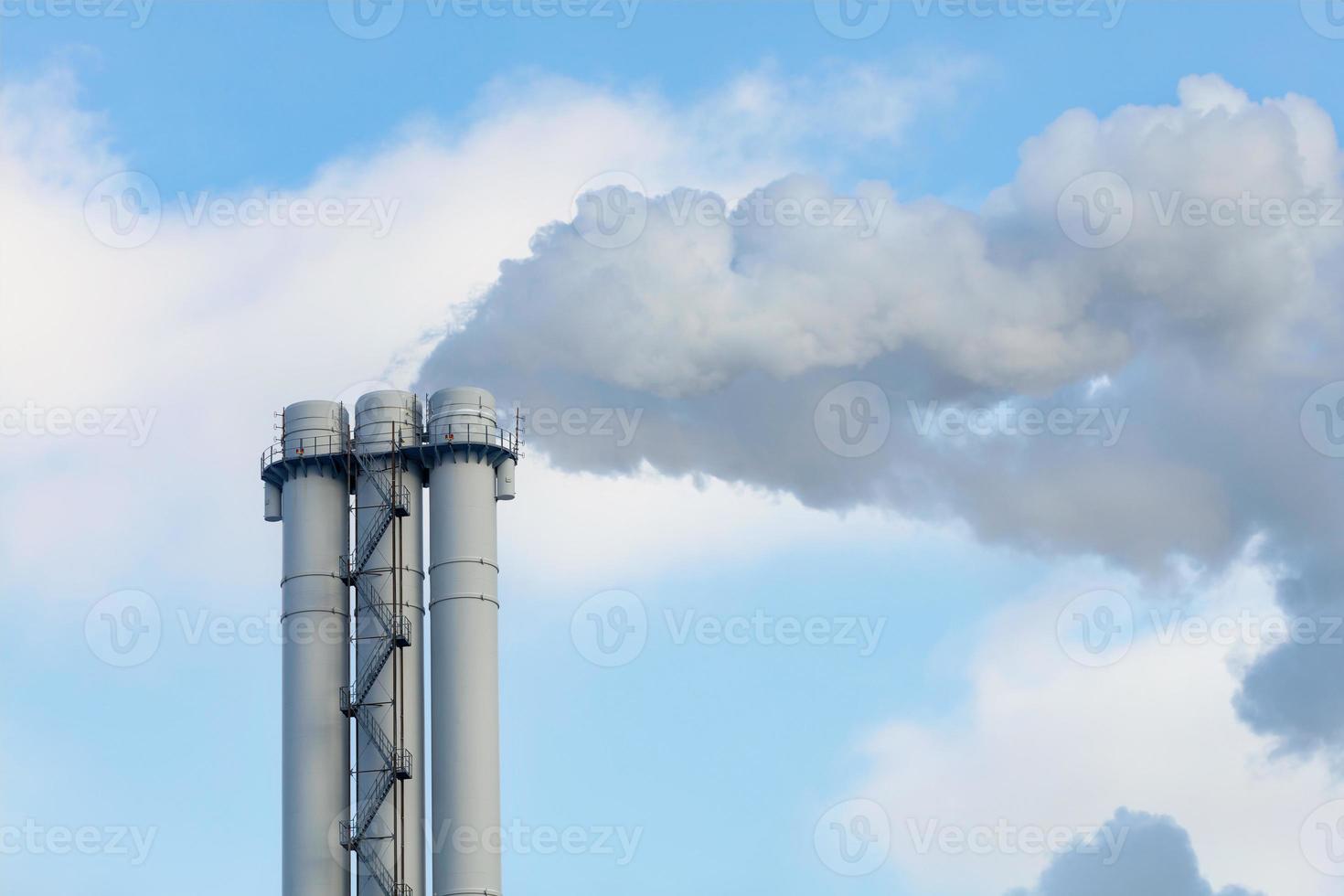 Emissions of smoke and steam from an industrial chimney into a clear sky. photo