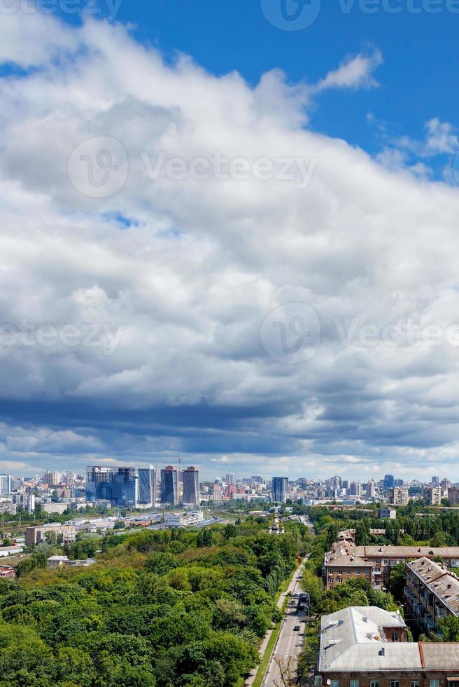 A large white and gray cloud loomed over a green park in the old residential area of the city and new buildings on the horizon against the backdrop of a bright summer day. photo