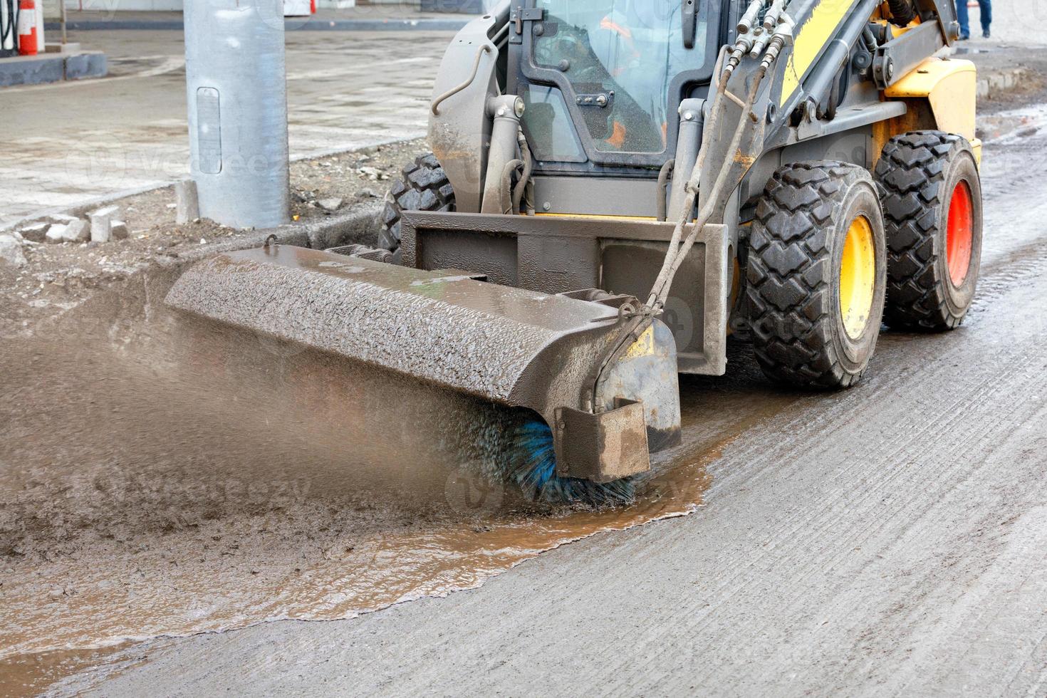 A compact road grader cleans a section of the road from dirty slurry with a nylon brush. photo