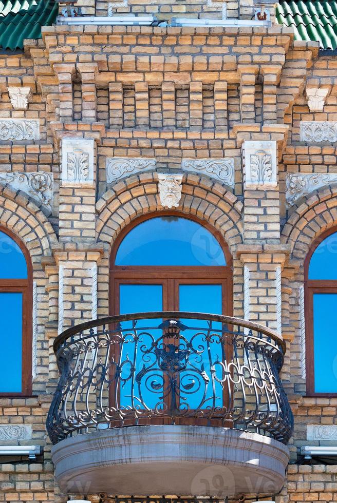 ventanas arqueadas con un hermoso y expresivo balcón en la fachada de ladrillos de la casa antigua y el reflejo del cielo azul en las vidrieras. foto