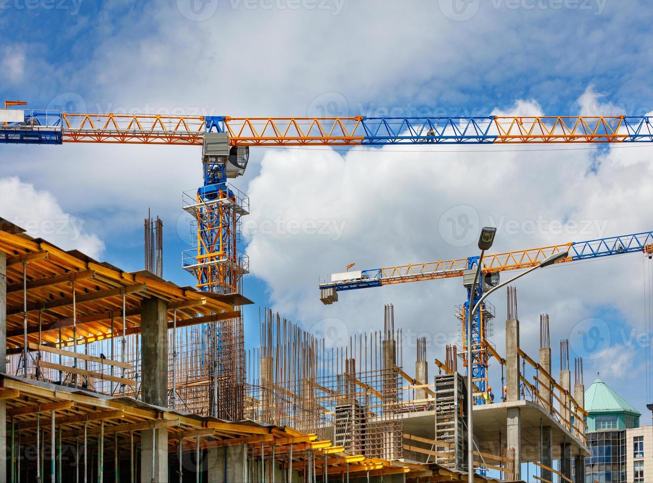 Modern building tower cranes are used in the construction of a building under construction against a blue, cloudy sky. photo