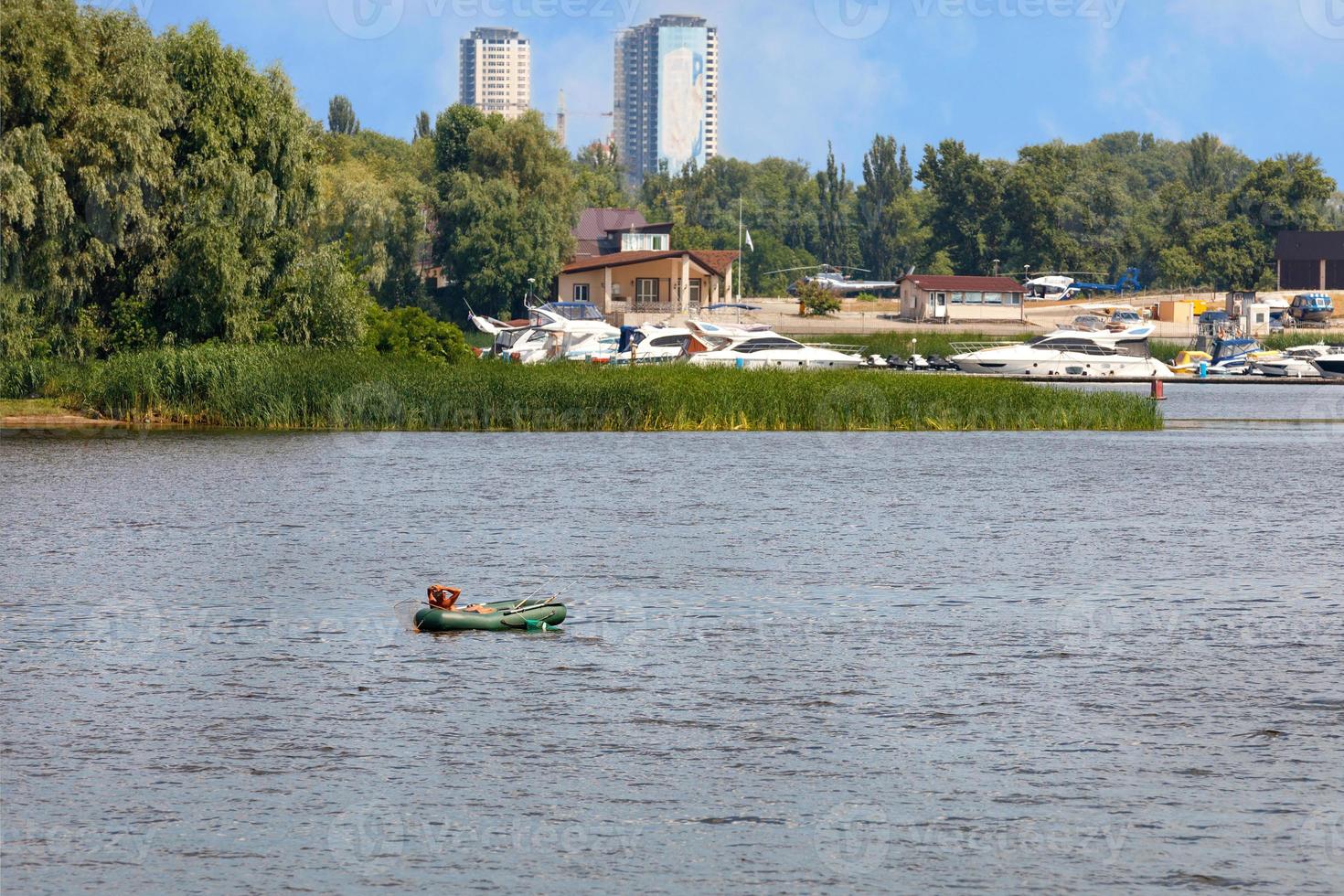 un pescador en un bote de goma inflable está pescando con cañas de pescar en medio del río en un día soleado de verano. foto