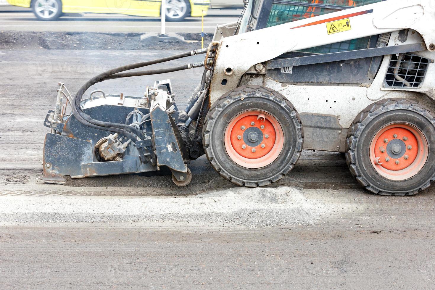 A bobcat with a surface repair attachment on asphalt plows the old surface on an asphalt road. photo