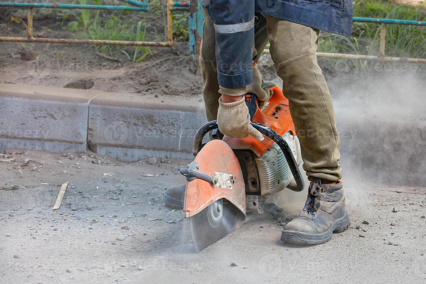 un trabajador usa una motosierra portátil y un disco de corte de diamante para cortar el asfalto viejo en la carretera. foto