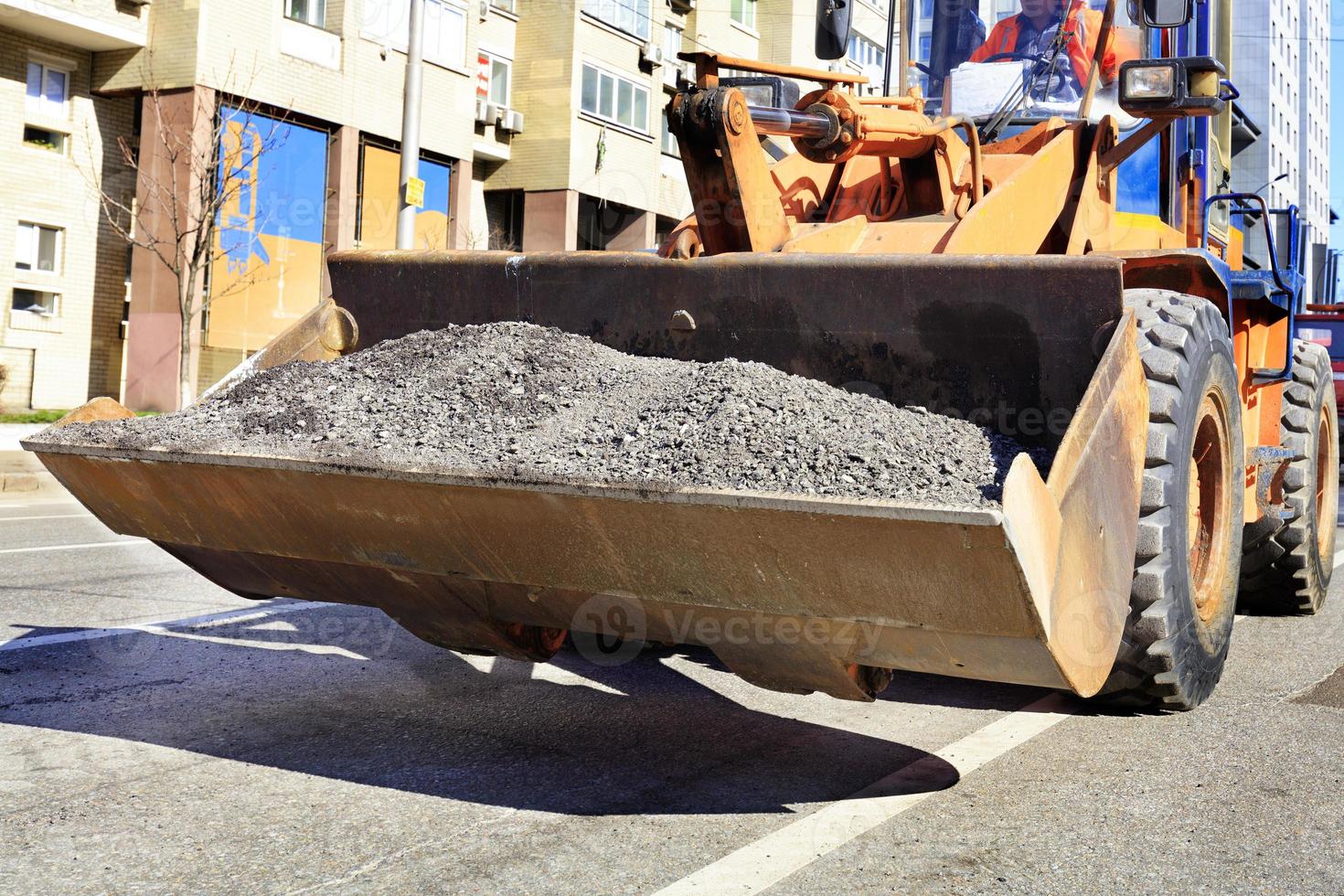 Heavy construction bulldozer carries in the bucket the old asphalt during the repair of the carriageway. photo