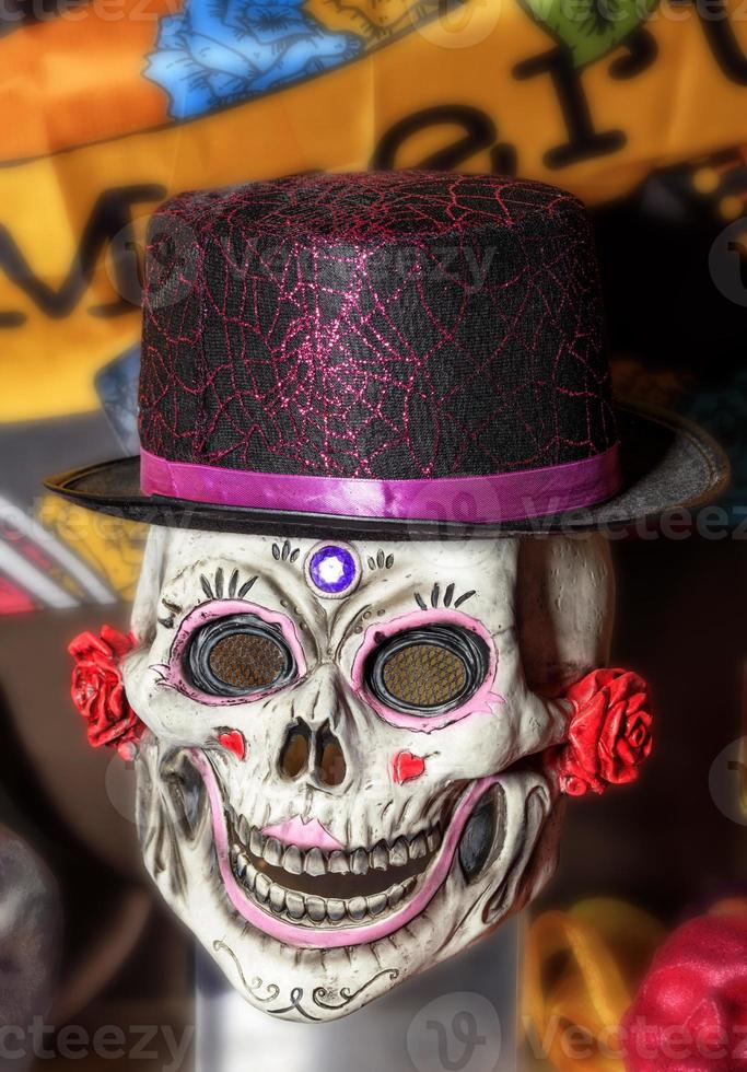 Halloween, skull doll with female makeup and a black-red hat, isolated on a blurred background. photo