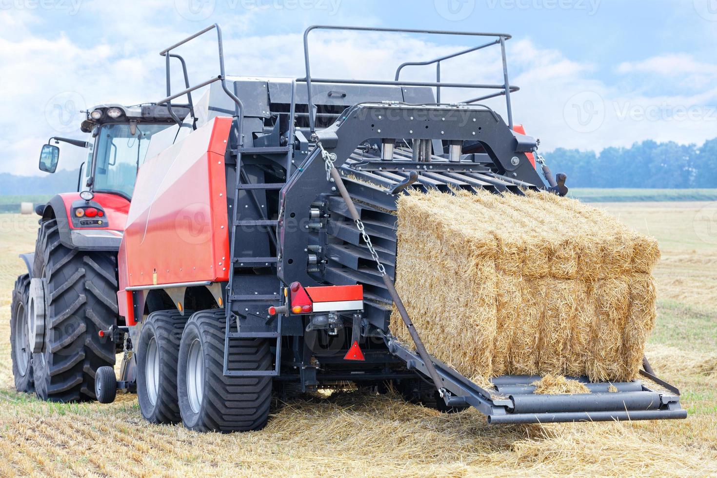 An agricultural tractor with a trailer forms bales of straw into dense briquettes in a wheat field. photo