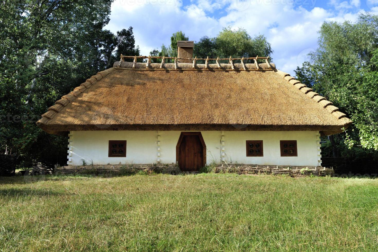 Old traditional Ukrainian rural house with thatched roof and wicker fence in the garden photo