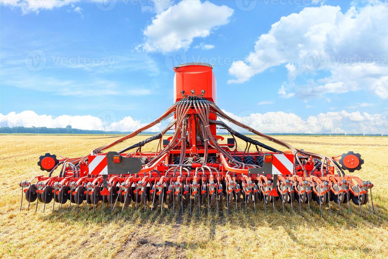 A multifunctional agricultural harrow stands in a harvested wheat field against a blue cloudy sky on a summer day. photo