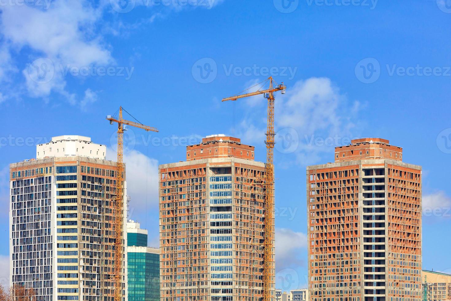 la construcción de modernos rascacielos residenciales con fachada de vidrio y grúas torre contra el cielo azul. foto