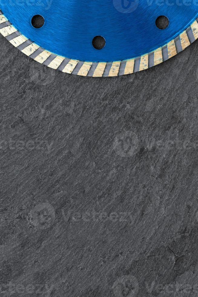 A fragment of a blue diamond cutting wheel is positioned on top against a background of gray granite. Close-up. Vertical image. photo