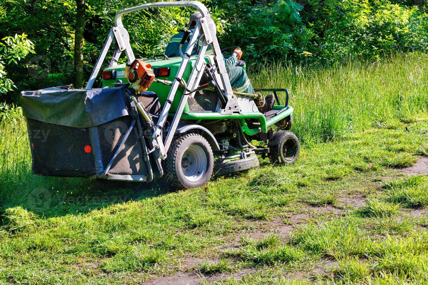 A professional tractor mower driven by a public utility worker climbs up the slope and mows tall grass. photo
