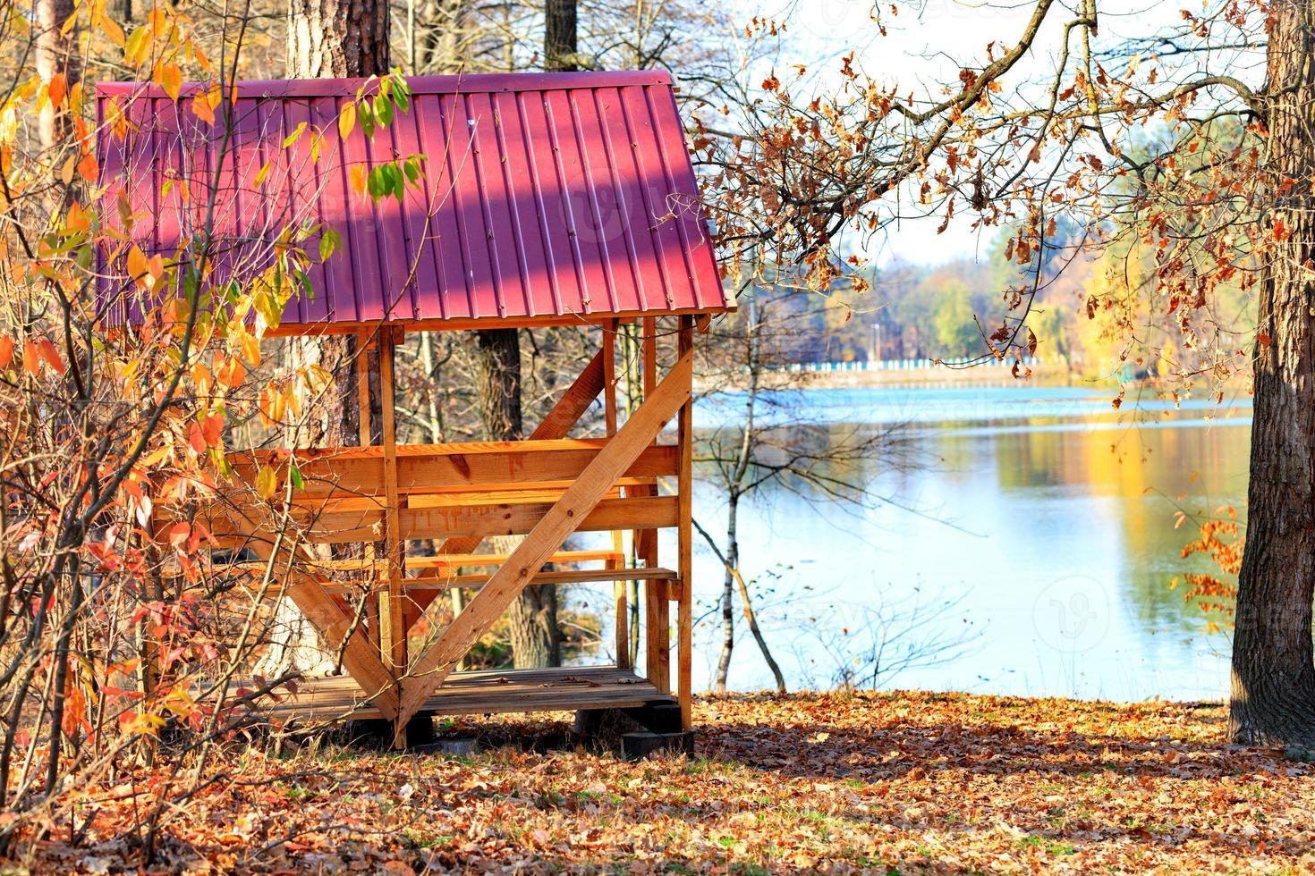 Wooden arbor with a table and picnic benches in the open air on the background of fallen leaves near a forest lake. photo
