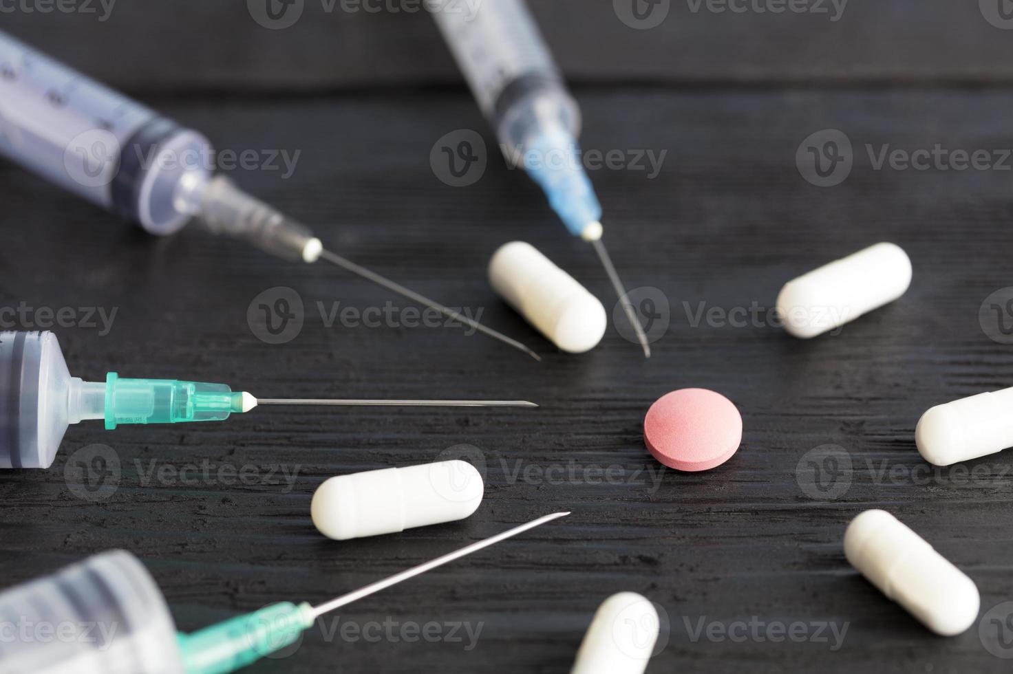 jeringas médicas de diversas capacidades, cápsulas, tabletas se encuentran en una vieja tabla de madera negra. foto