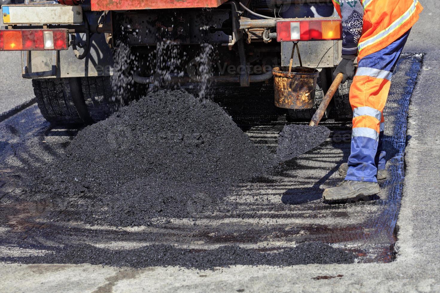 El trabajador de la carretera distribuye un trozo de asfalto con una pala para reparar la carretera. foto