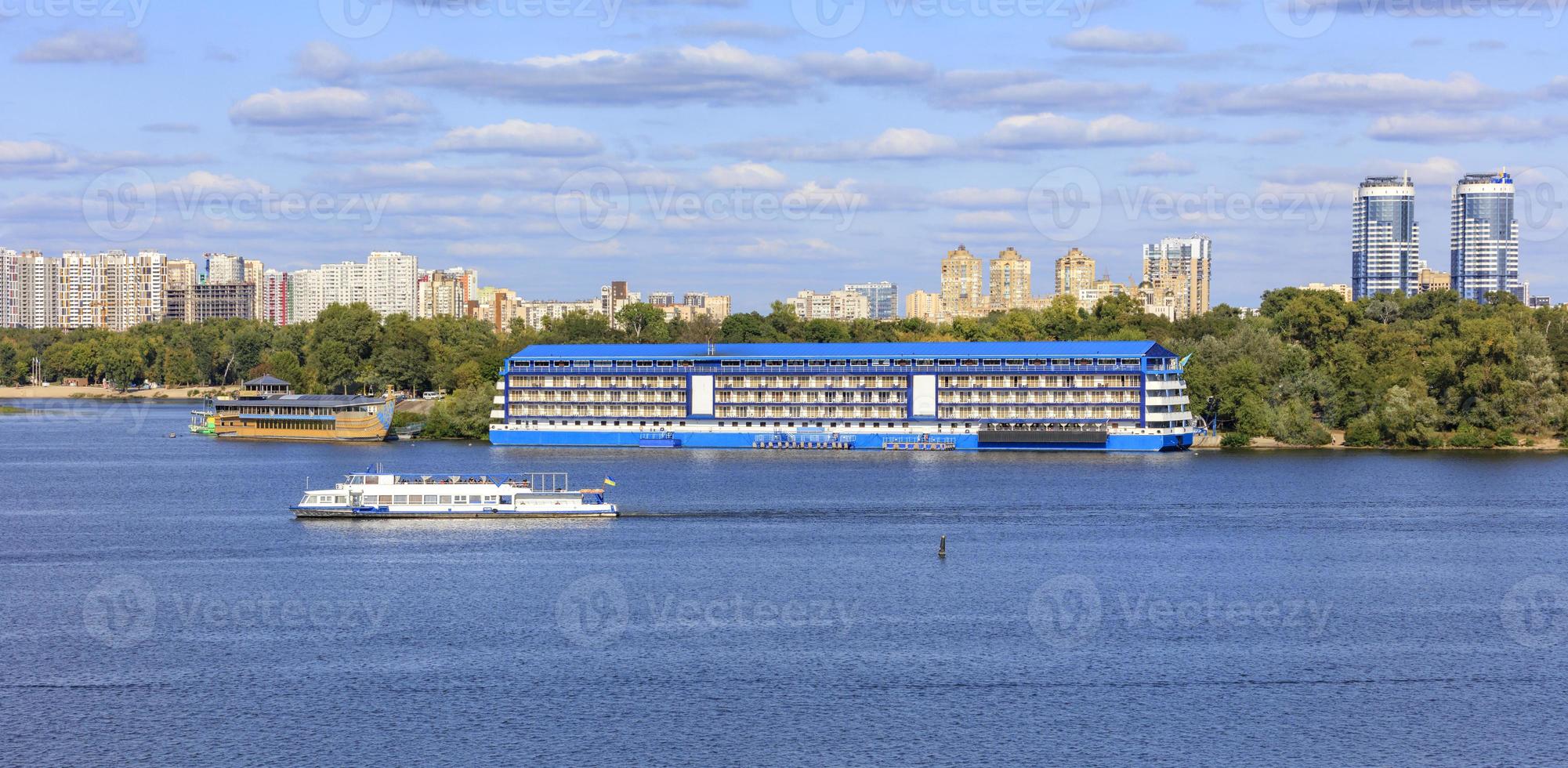 Landscape, pleasure ships go along the Dnipro River against the background of residential areas of Kyiv on the banks in bright sunlight. photo