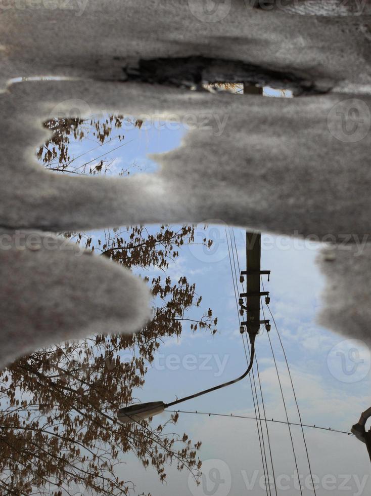 reflejo del cielo, la silueta de una farola y un árbol en un charco sobre mal asfalto. foto