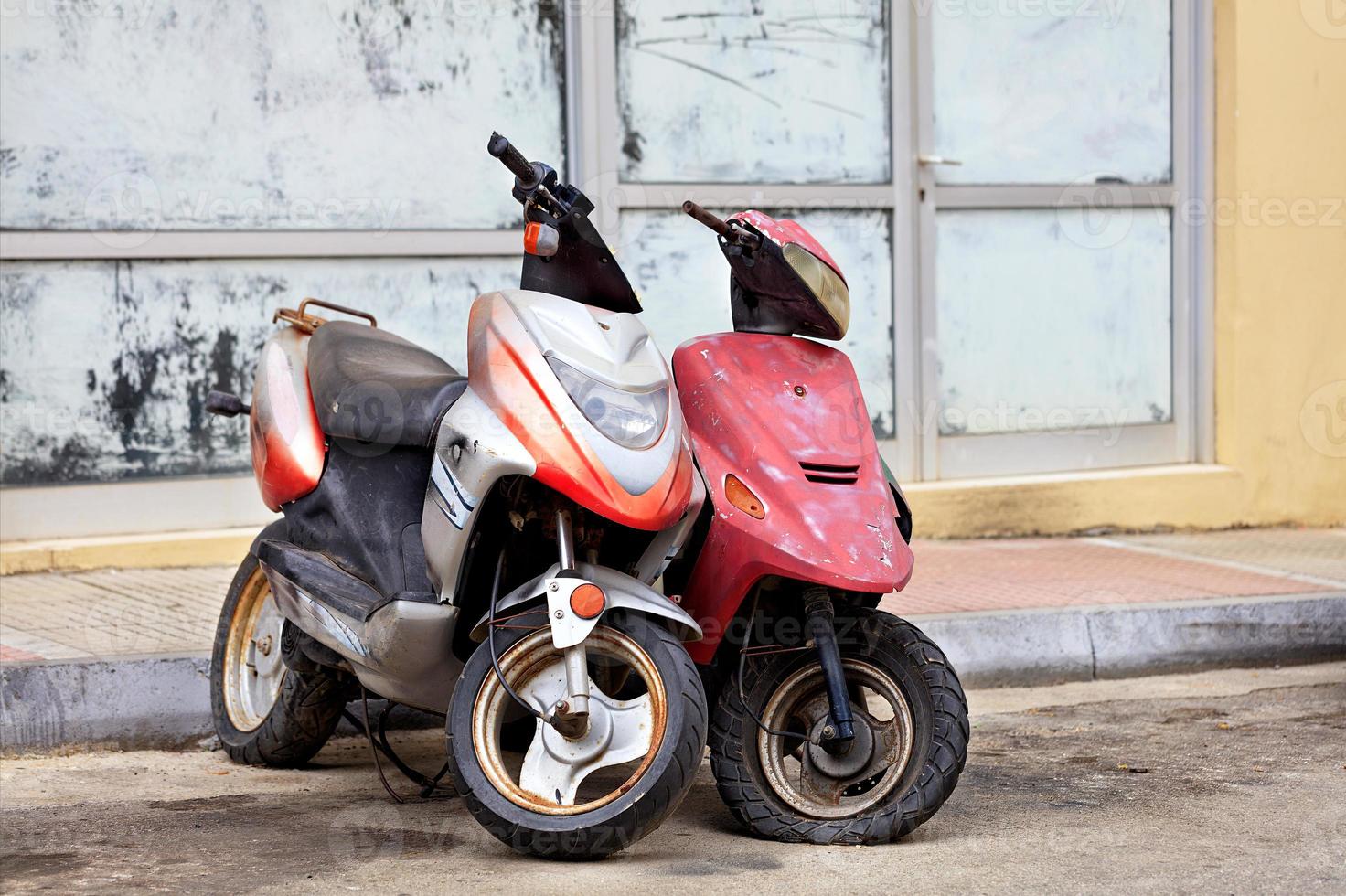 Two old worn mopeds stand alone at the edge of the road. photo