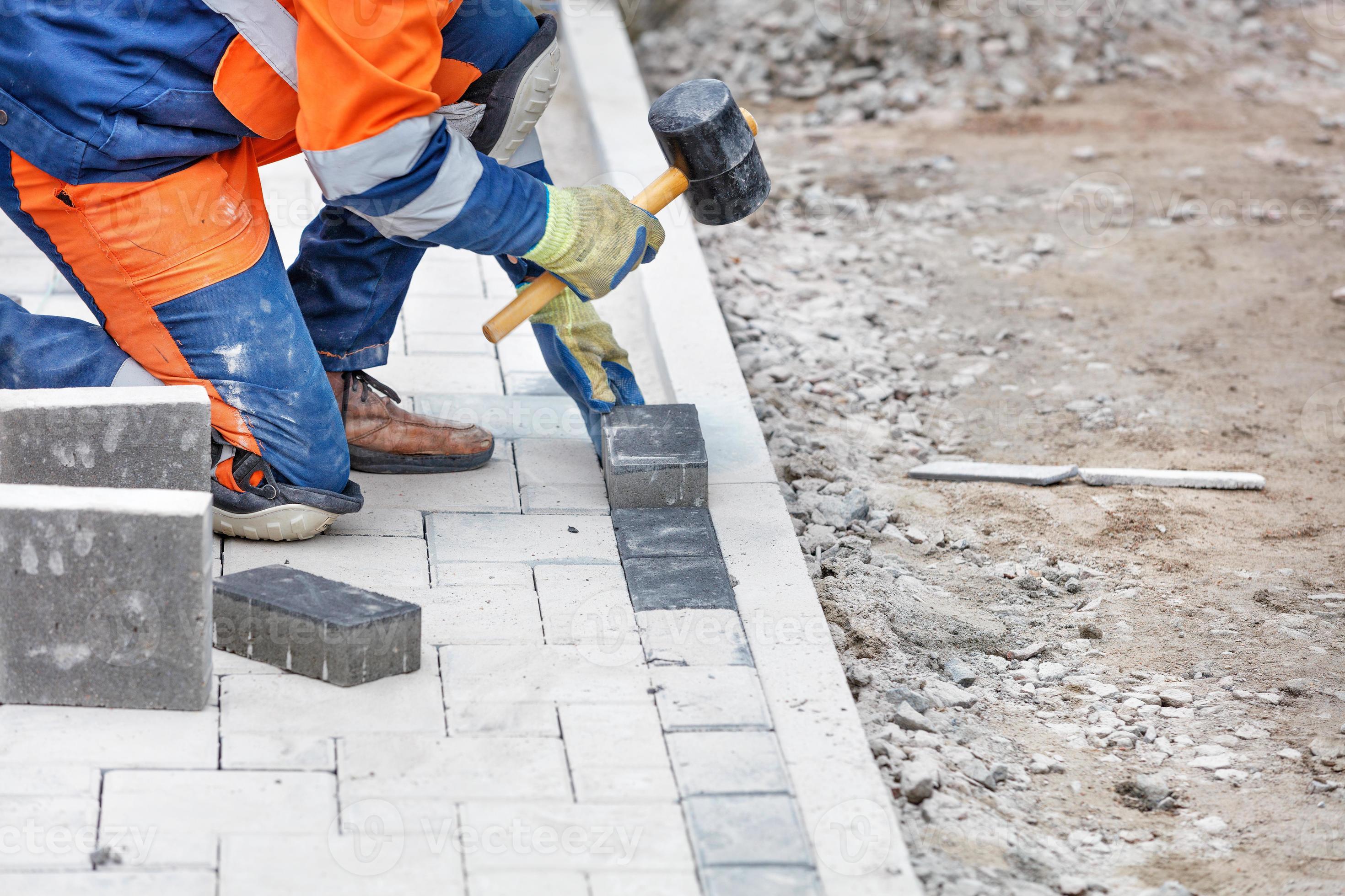 A worker hammers in the paving slabs of the work site with a