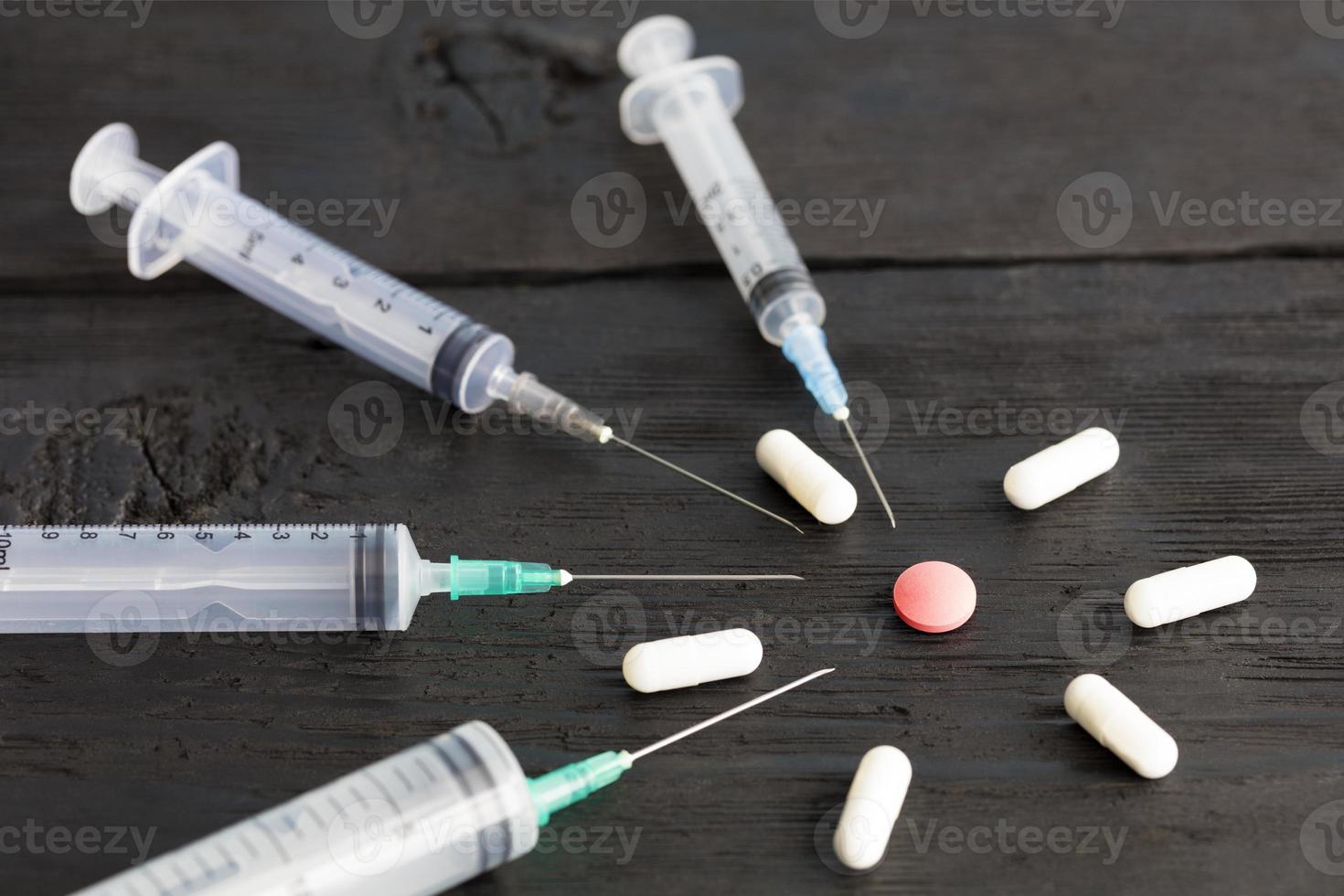 Medical syringes of various capacities, capsules, tablets lie on an old black wooden board. photo