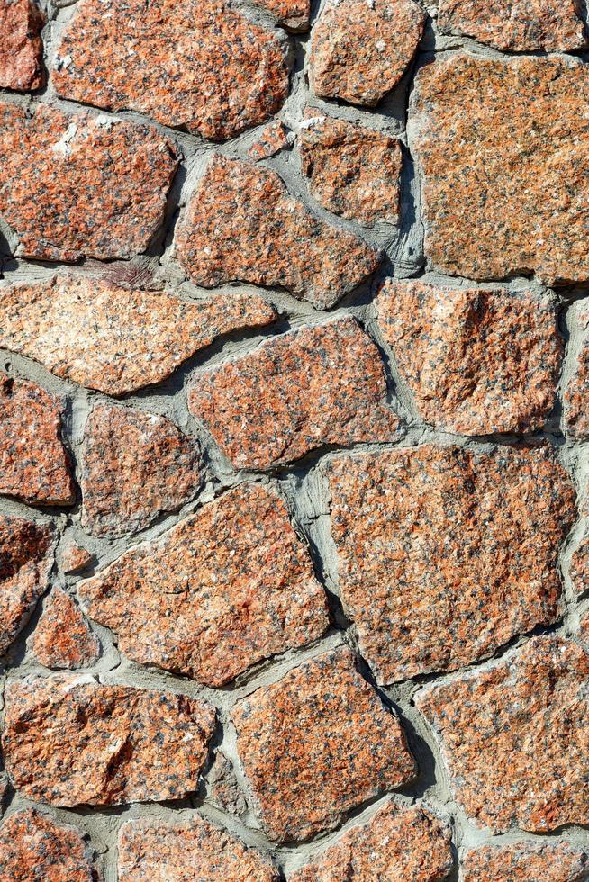 la textura de la pared está forrada con cantos rodados de granito rojo a la luz del sol. imagen vertical. foto