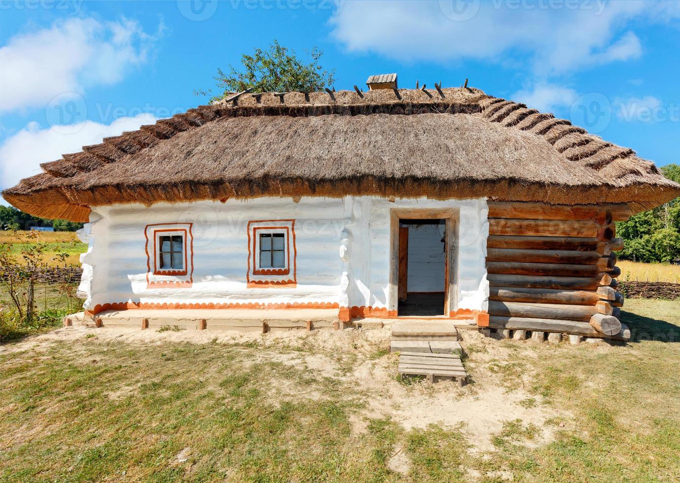 Fachada de una antigua casa rural tradicional ucraniana con techo de paja en un día de verano contra un cielo azul. foto