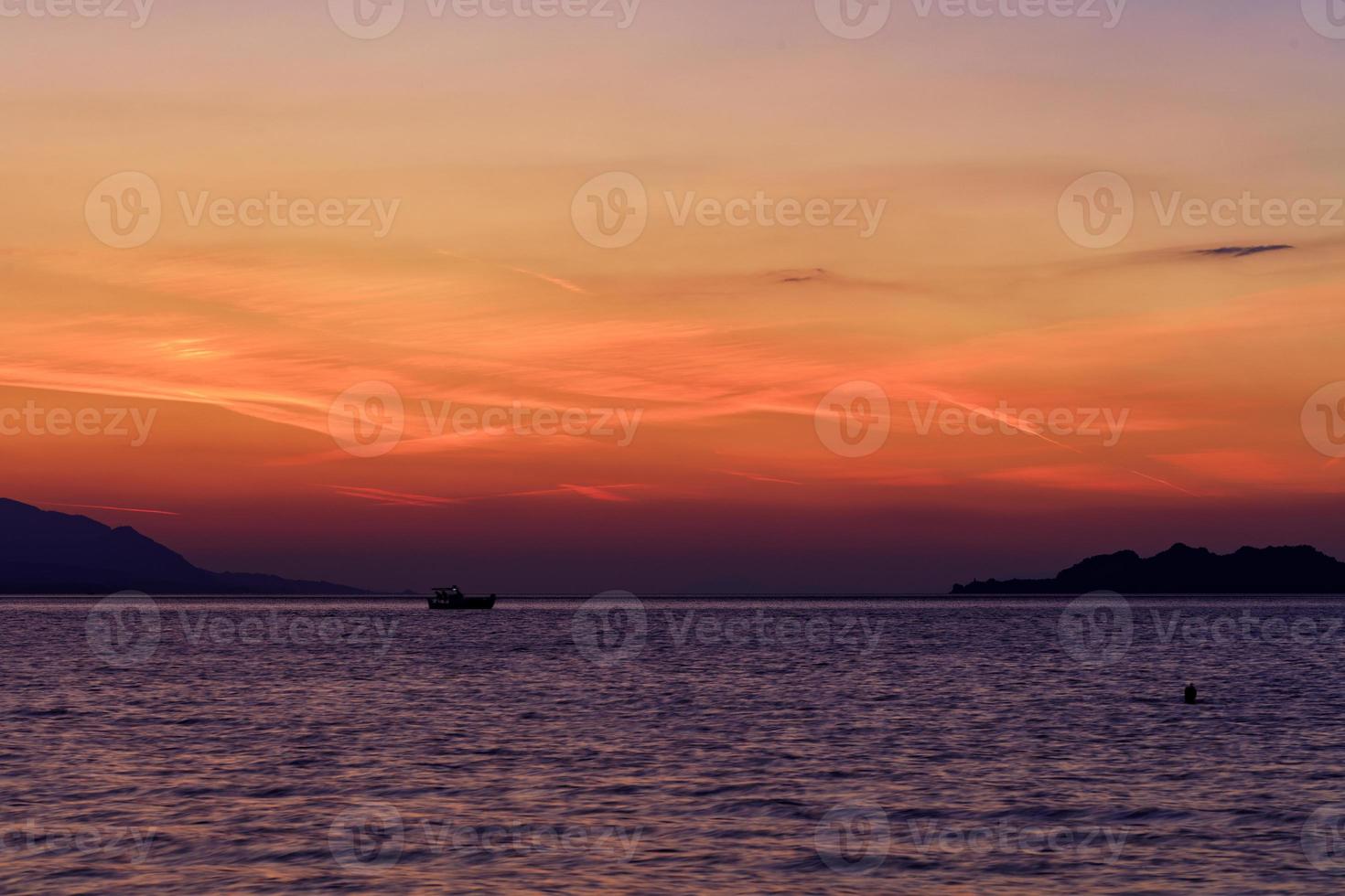 silueta de un barco de mar que recorre el horizonte de la línea del mar con el telón de fondo de una hermosa y vibrante puesta de sol en el golfo de corinto. foto