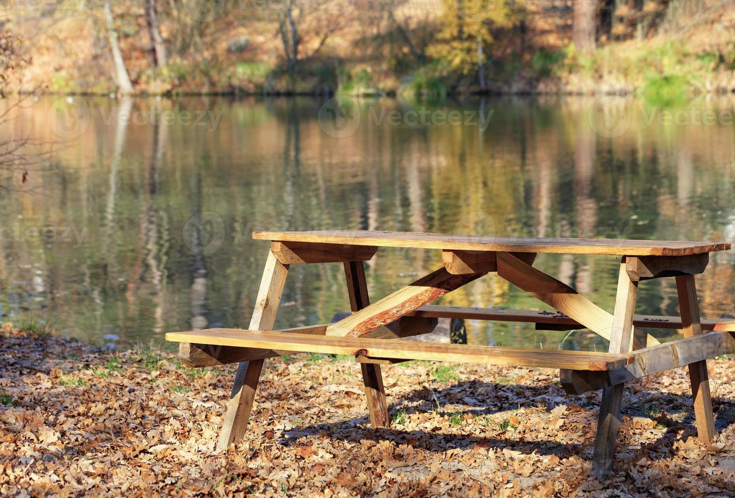 Wooden table with picnic benches in the open air on the background of fallen oak leaves near a forest lake. photo