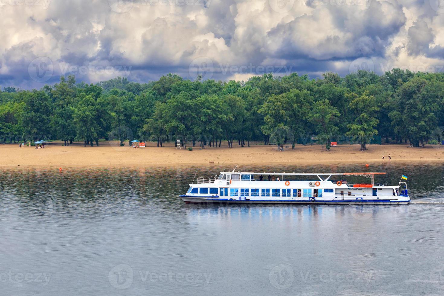 A river tram runs along the banks of the Dnipro against the backdrop of a deserted beach in anticipation of an impending thunderstorm. photo