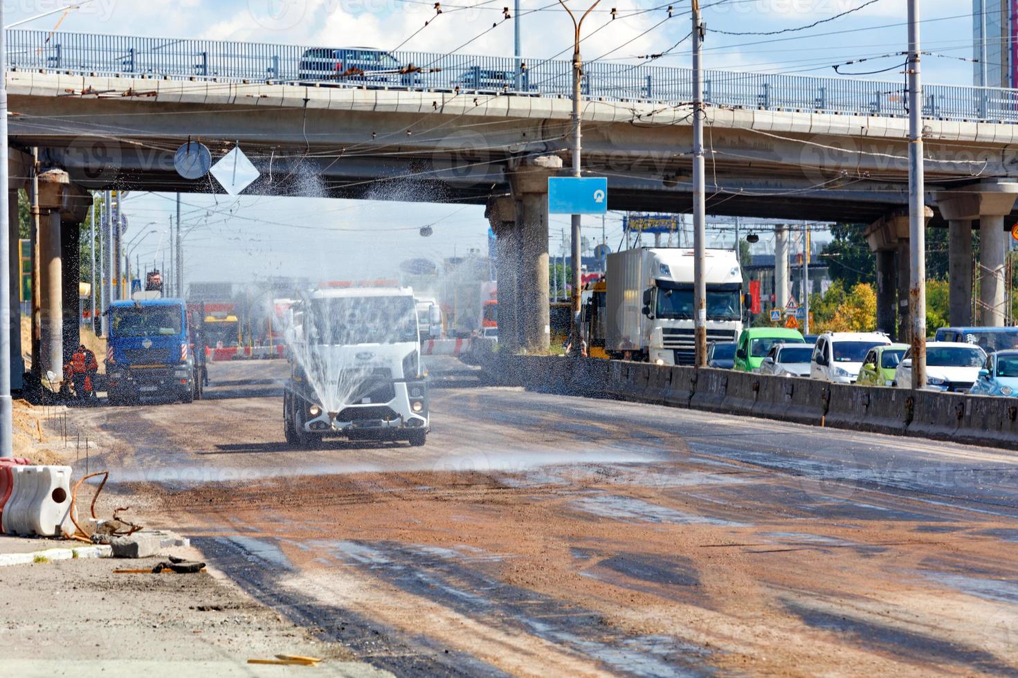 Las máquinas de riego riegan una sección de trabajo de la carretera en un día caluroso y soleado. foto