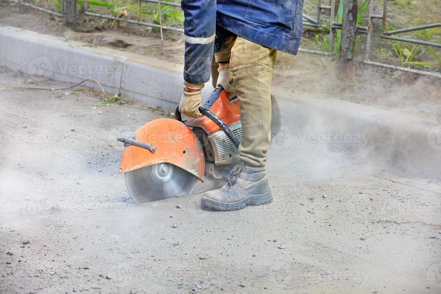 Un trabajador de la construcción que usa una sierra de gasolina portátil corta asfalto viejo para reparar un sitio en la carretera. foto