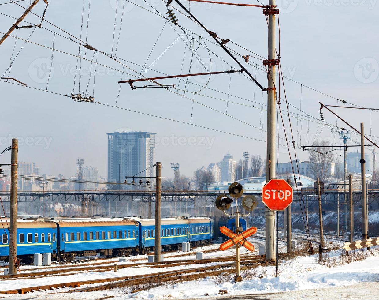 Red stop sign at the railway crossing against the background of the railway station and buildings of the winter city. photo